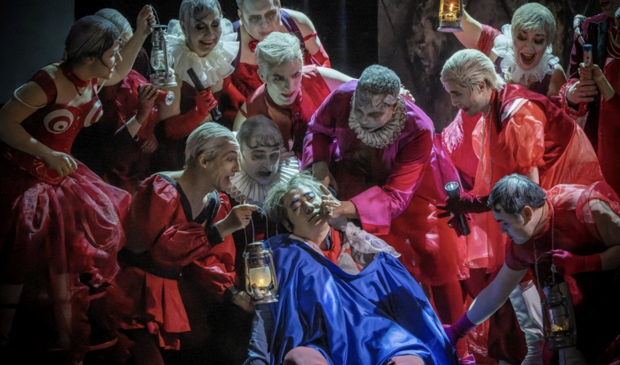 Rigoletto liegt im blauen Umhang inmitten des rot gekleideten Hofstaates.
